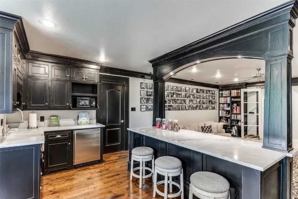 Dark painted bar with an arched opening, beverage fridge and counter seating