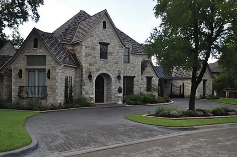 Stone home with a steep roof set behind a curving paver drive