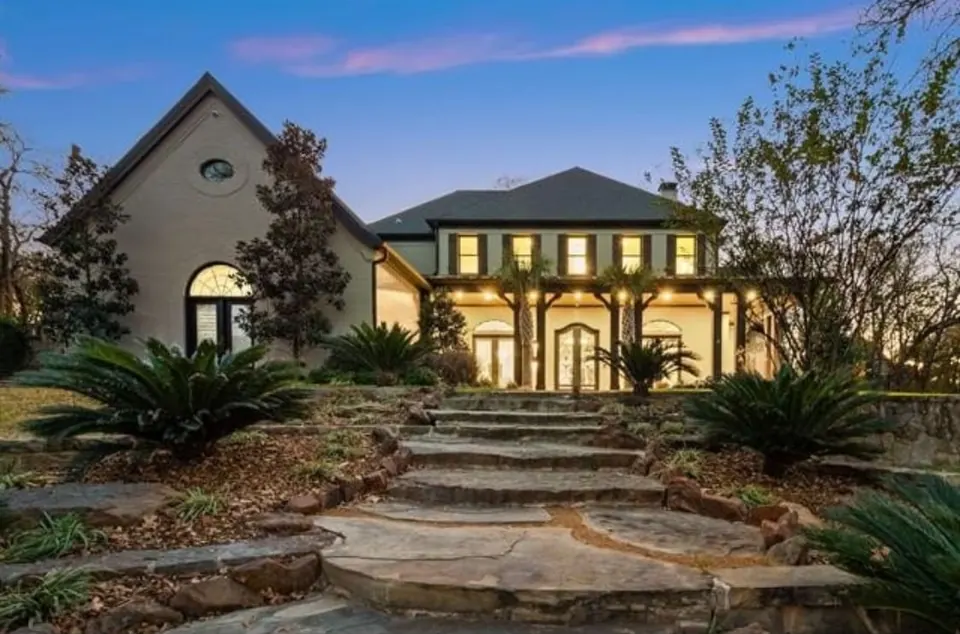 Stone home lit at dusk, reached by flagstone steps through landscaped beds