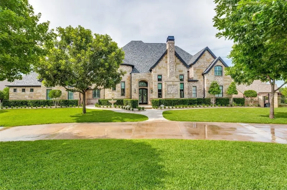 Wide view of a stone home with steep gables, a circular drive and mature trees