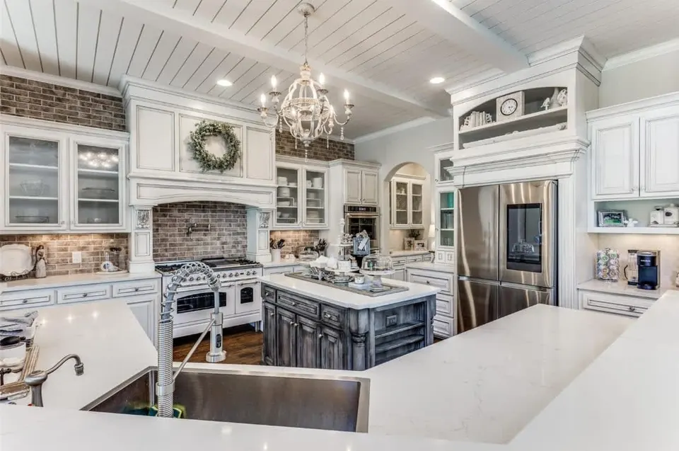 White kitchen with a large island, a brick-backed range alcove and two chandeliers