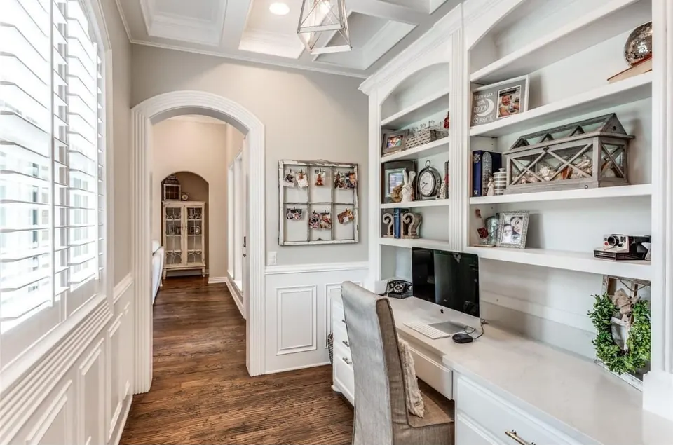 Home office with a built-in desk, floor-to-ceiling shelving and an arched hallway
