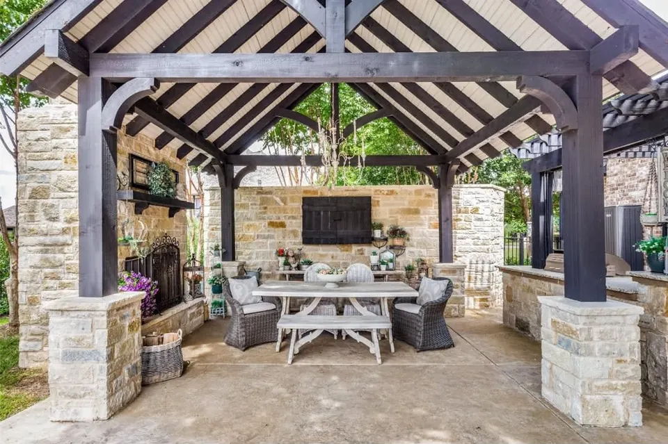 Timber-framed outdoor pavilion with stone columns, a fireplace and a dining table