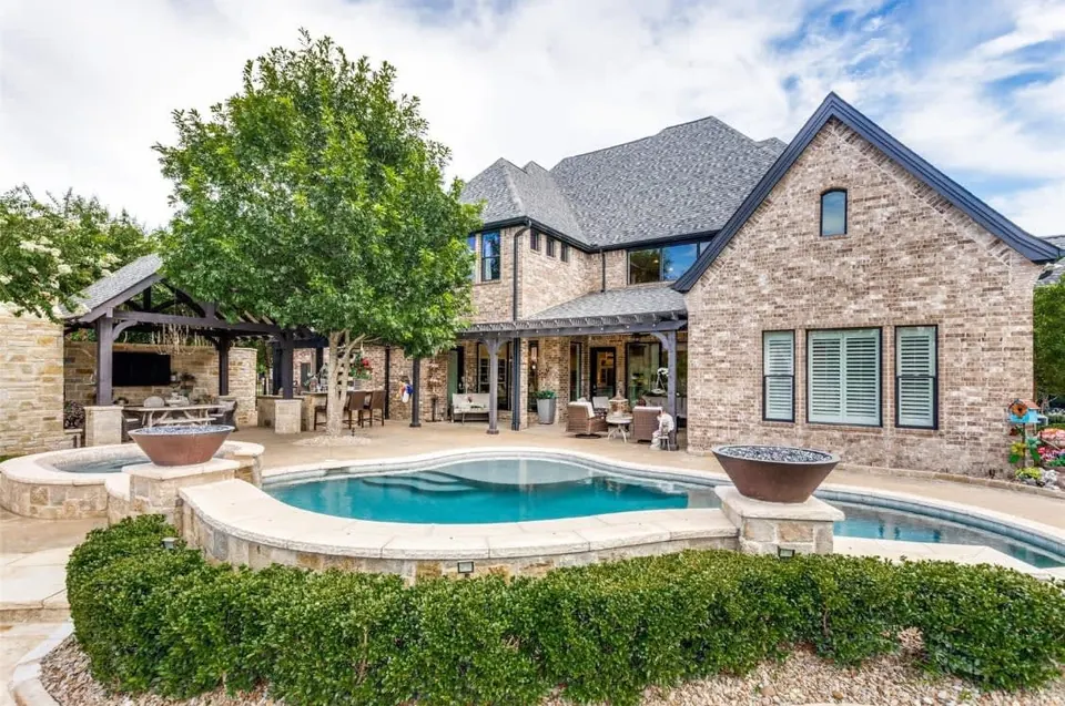 Rear of a brick and stone home with a pool, spa, fire bowls and a covered patio