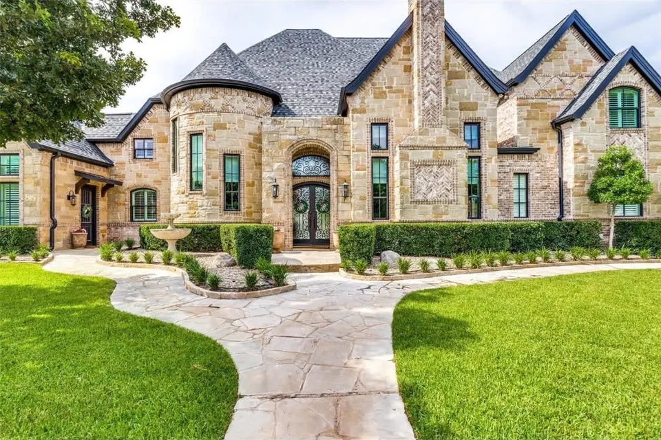 Two-story stone and brick home with a round turret, arched iron entry doors and a flagstone walk