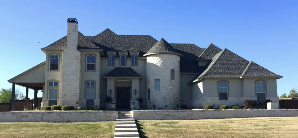 Stucco and limestone home with a round stone turret above a raised front lawn