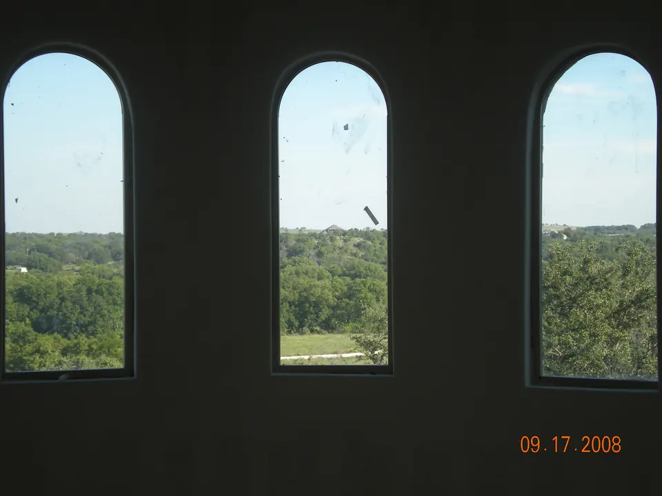 Three arched windows framing a wooded view from an unfinished upper room