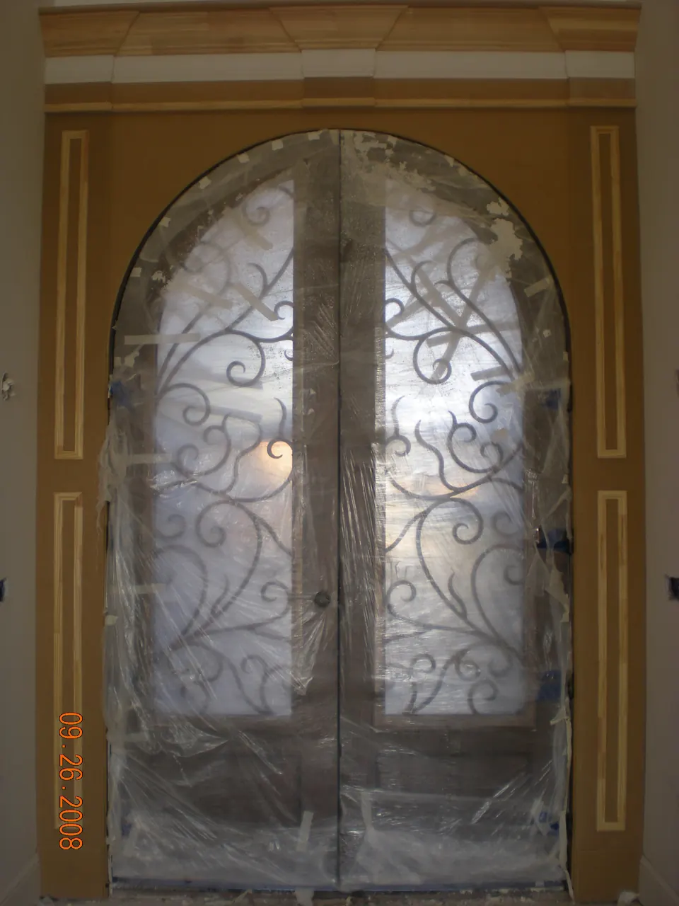 Arched wrought iron double doors installed and still wrapped in protective plastic