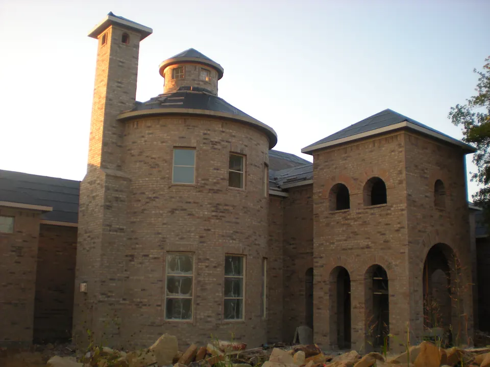 Brick house under construction with a round turret, a tall chimney and arched openings