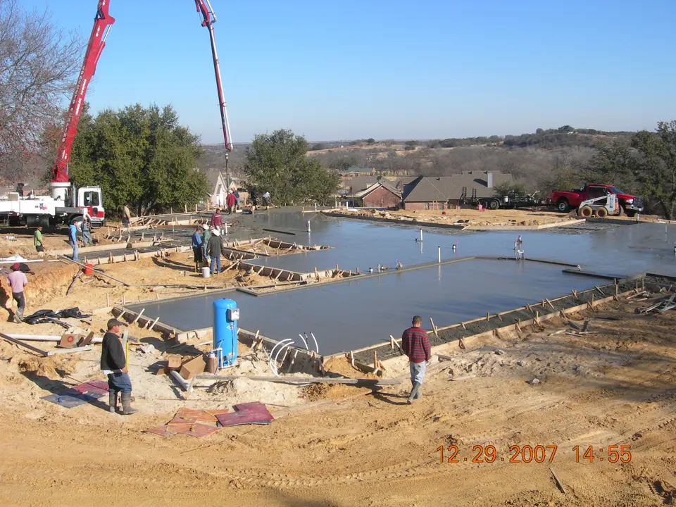 Crew finishing a large concrete slab foundation while a pump truck boom places concrete
