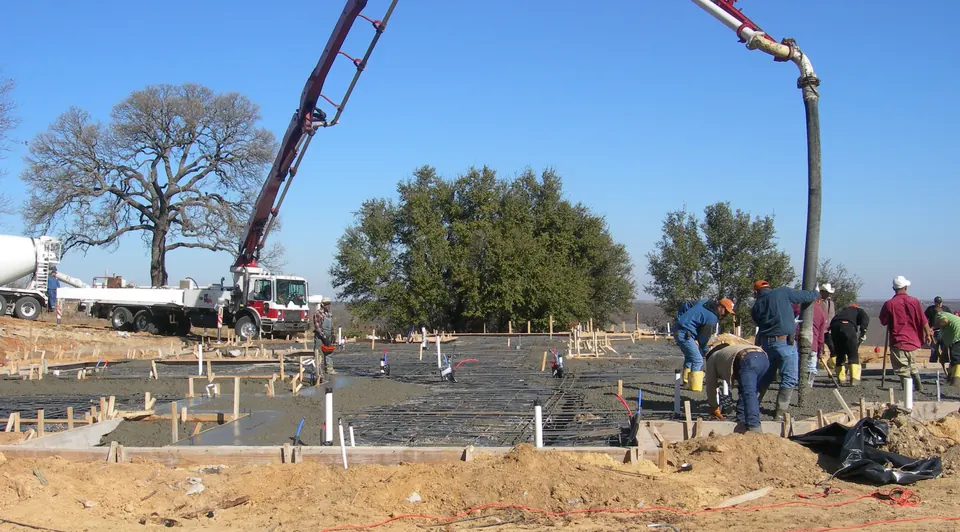 Concrete pump boom over a crew placing a slab foundation under a clear sky