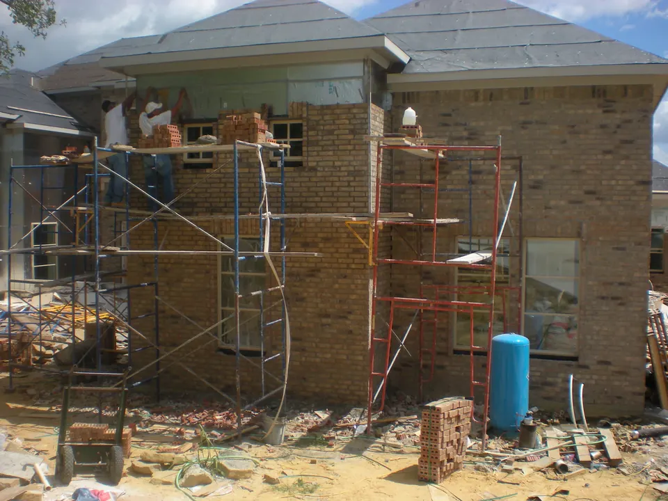 Masons on scaffolding laying brick around the windows of a house under construction