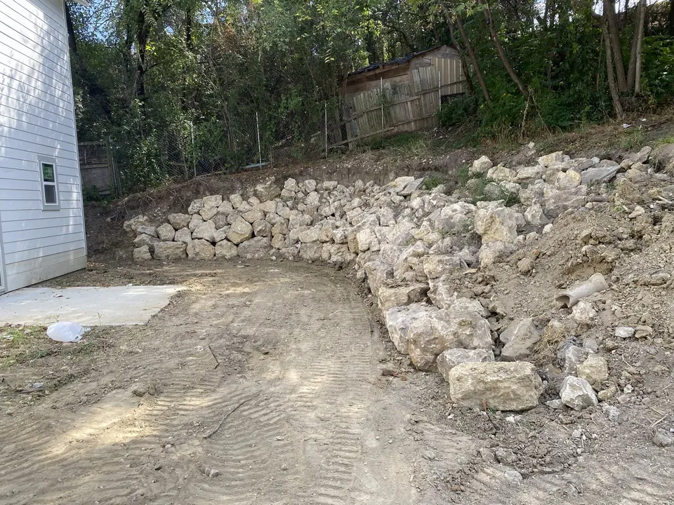 Limestone boulder retaining wall stacked along the edge of a graded lot