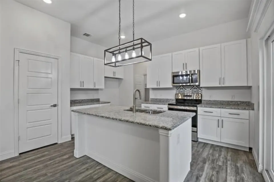 Kitchen with white shaker cabinets, a granite island and a black pendant light
